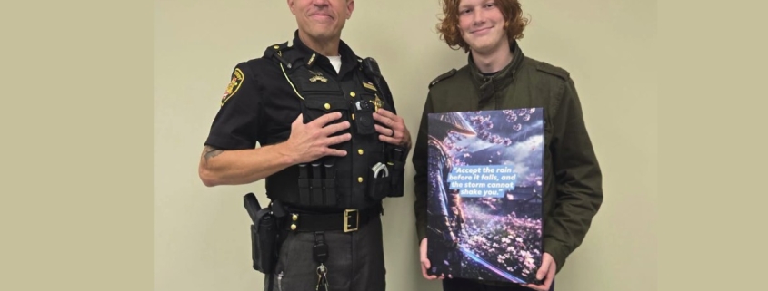 Fostoria News Police officer and young man holding a book together in an indoor setting.